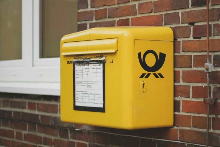 Gelbe Briefkasten an einer Ziegelsteinmauer mit Logo der Deutschen Post.