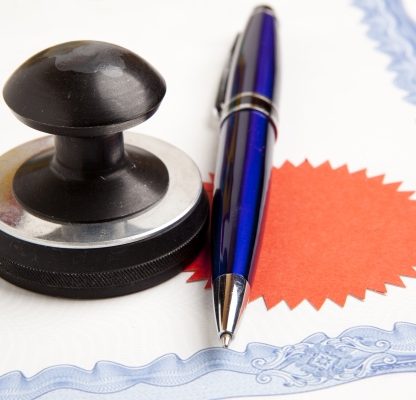 Schwarzer Stempel und blauer Stift neben einem Dokument mit rotem Siegel.