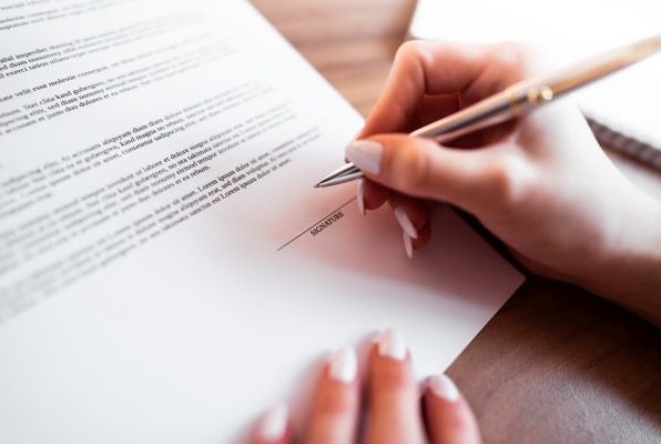 Eine Hand mit einem Stift schreibt auf einem Blatt Papier mit Text.