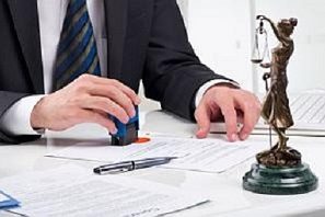 Ein Anwalt stempelt Dokumente neben einer Justitia-Statue auf einem Tisch.