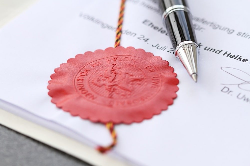Rotes Wachssiegel mit Schriftzug, daneben ein Kugelschreiber auf Papier.